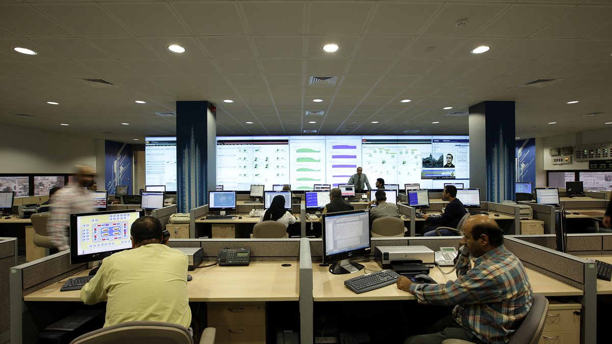 Engineers at workstations monitoring systems in a network operations centre with a large video wall